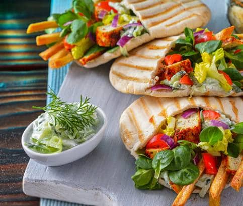 Veganský tofu gyros v pitě, podávaný s cuketovými chipsy a veganskými tzatziki