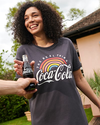Dark grey T-shirt dress. Front features the words the real thing above a rainbow, above a large Coca-Cola logo.