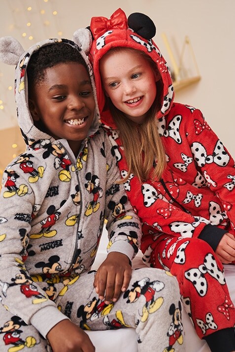 Mickey onesie in light grey with an all-over Mickey mouse print and hood with mouse ears. Minnie onesie in red with white, red and pink bow print and a hood with mouse ears.