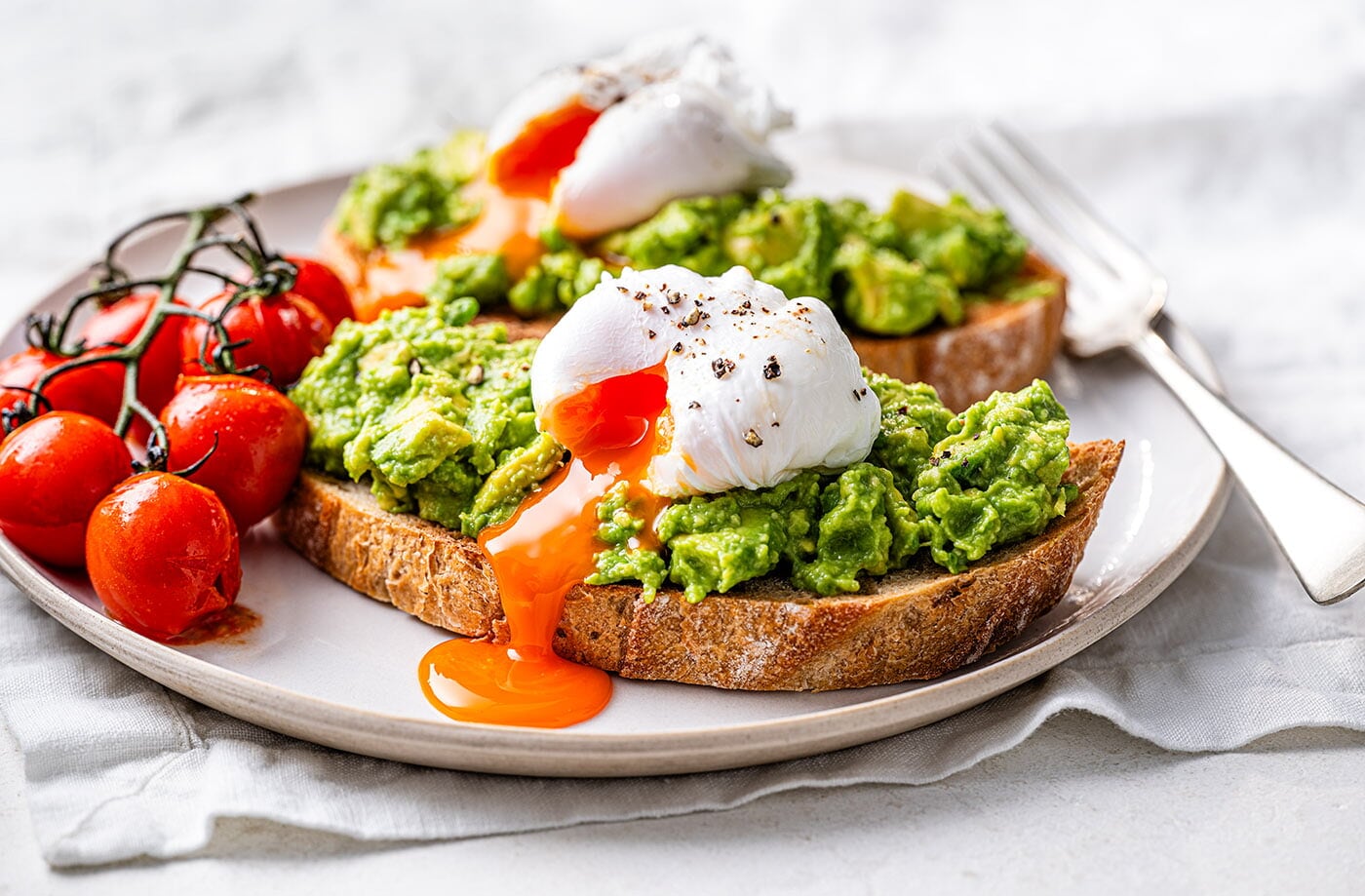 Smashed avocado on toast with poached eggs and tomatoes